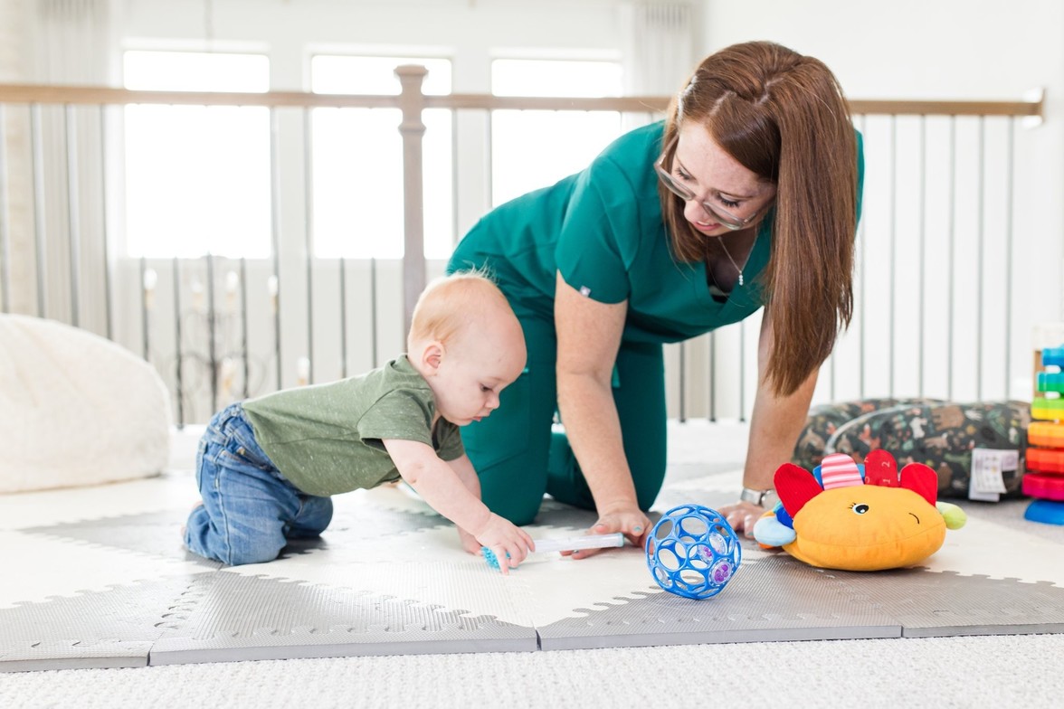 Baby crawling on hands and knees, looking at Physical Therapist.